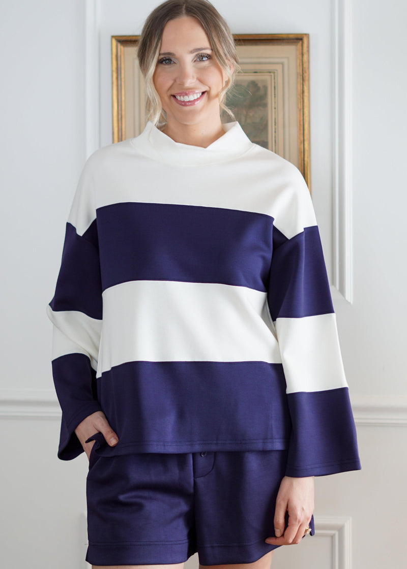 Woman wearing a navy and white striped sweater with shorts indoors.