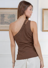 Woman wearing a brown one-shoulder top in an indoor setting with framed pictures on the wall.